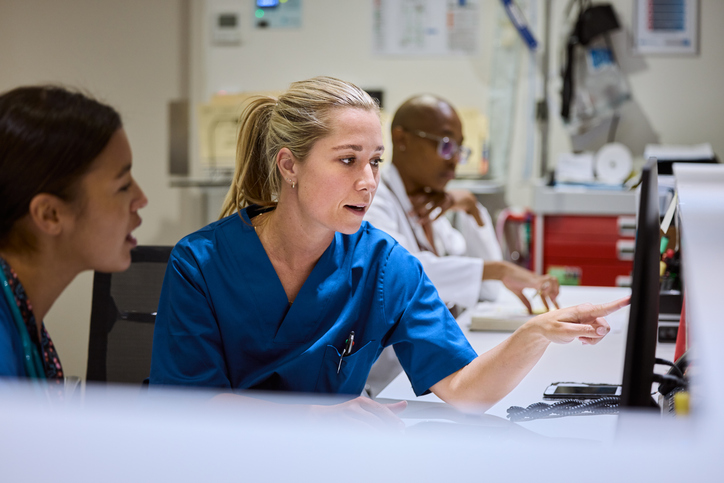 Two nurses discussing strategy over a computer monitor.